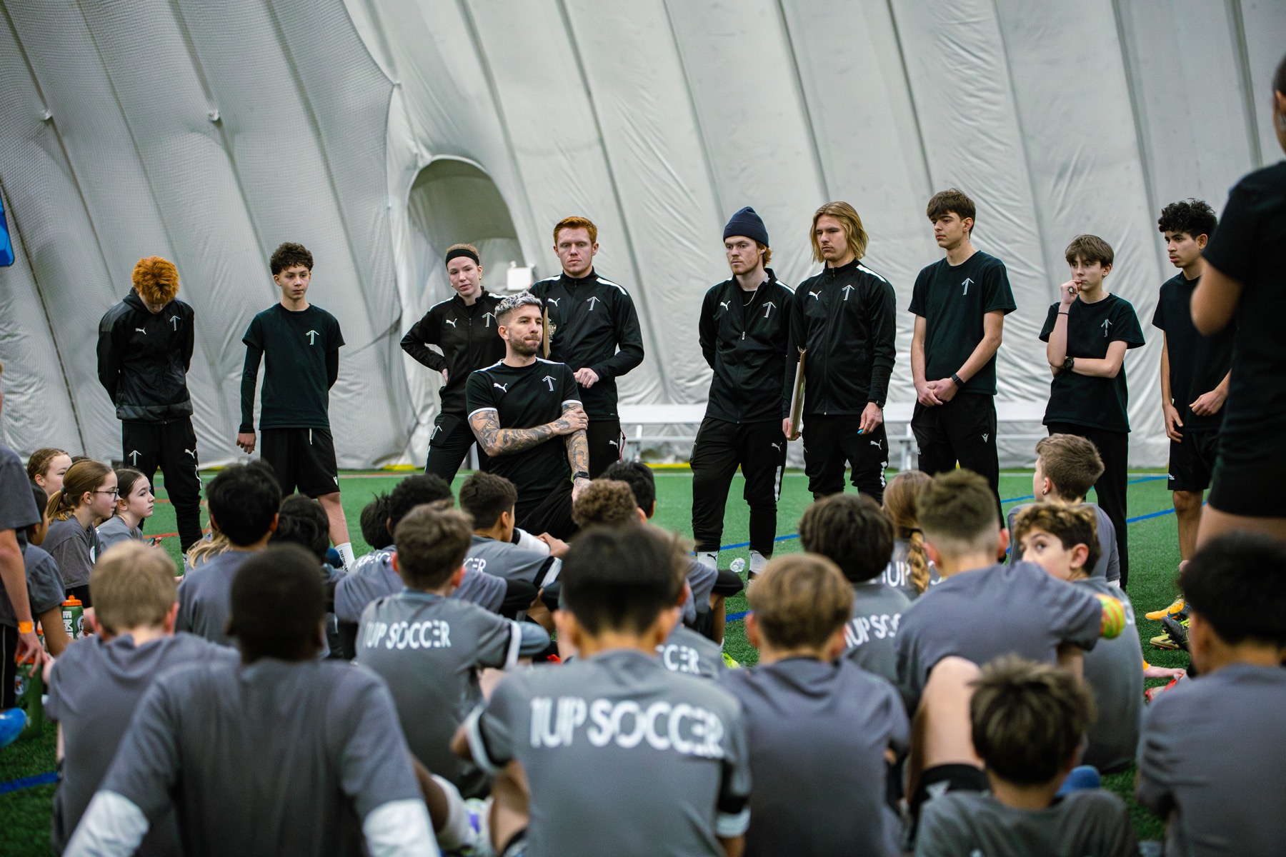 1UP Soccer coaching staff addressing a group of players at an indoor facility in Calgary