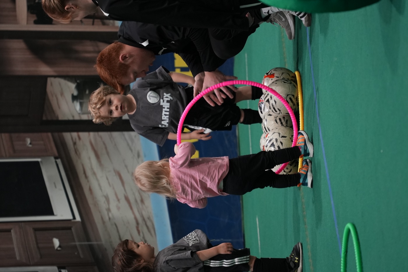 A 1UP coach kneeling with three Mini 1uppers and a hoop at an indoor session